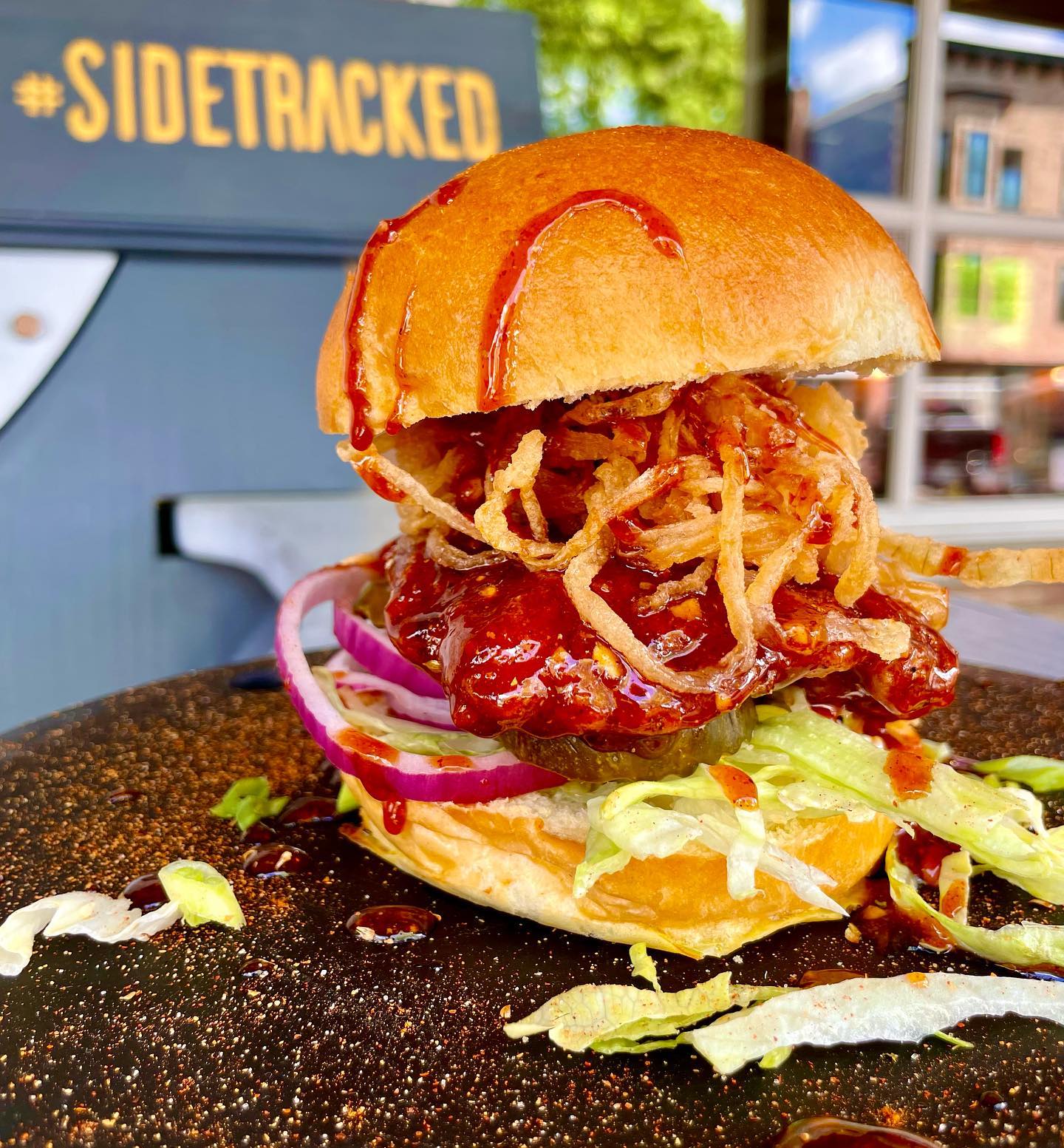 A close up of a hamburger on a plate with a sign in the background that says sidetracked
