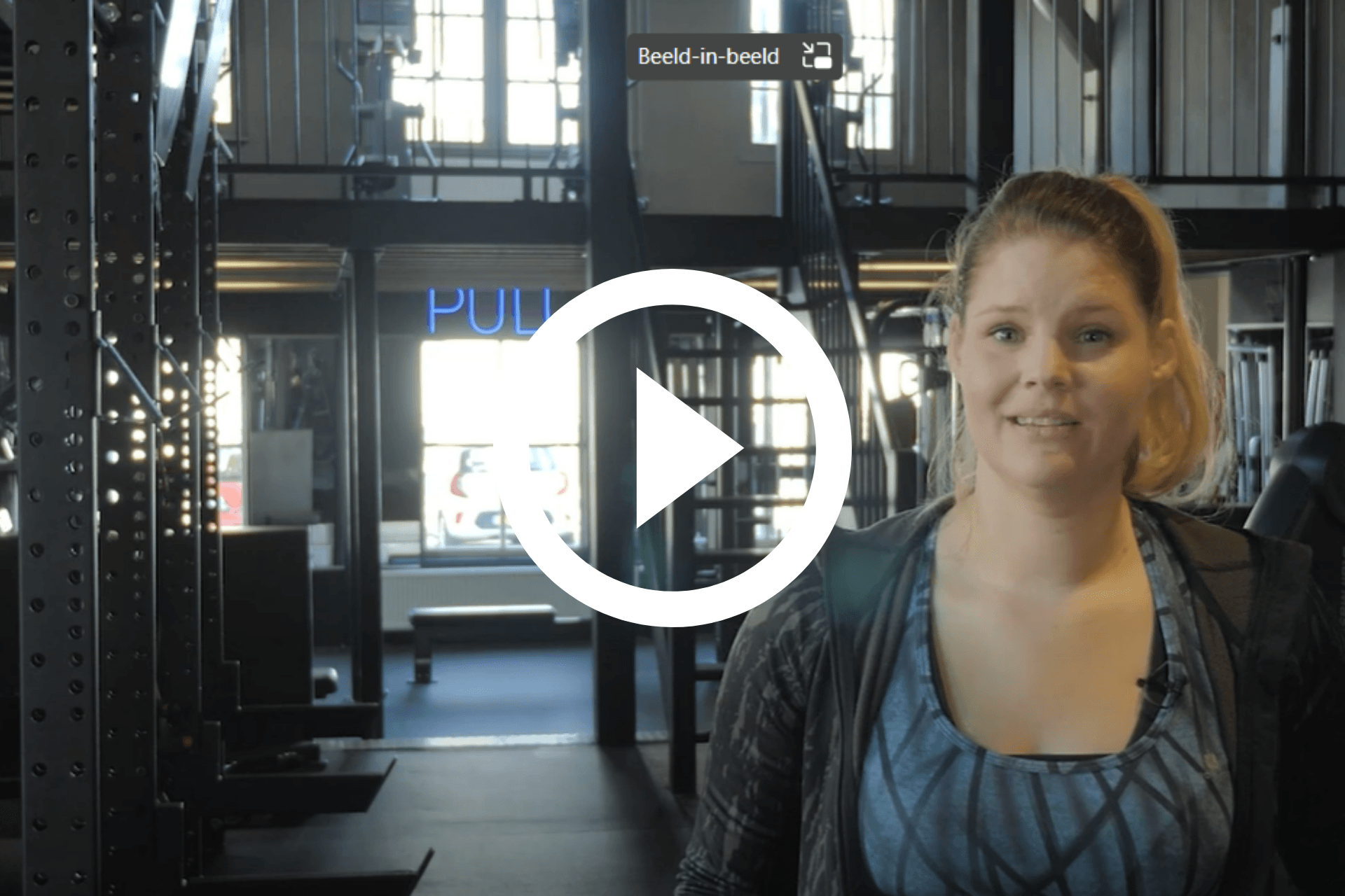 Vrouw staat in een sportschool, met fitnessapparatuur en grote ramen achter haar.