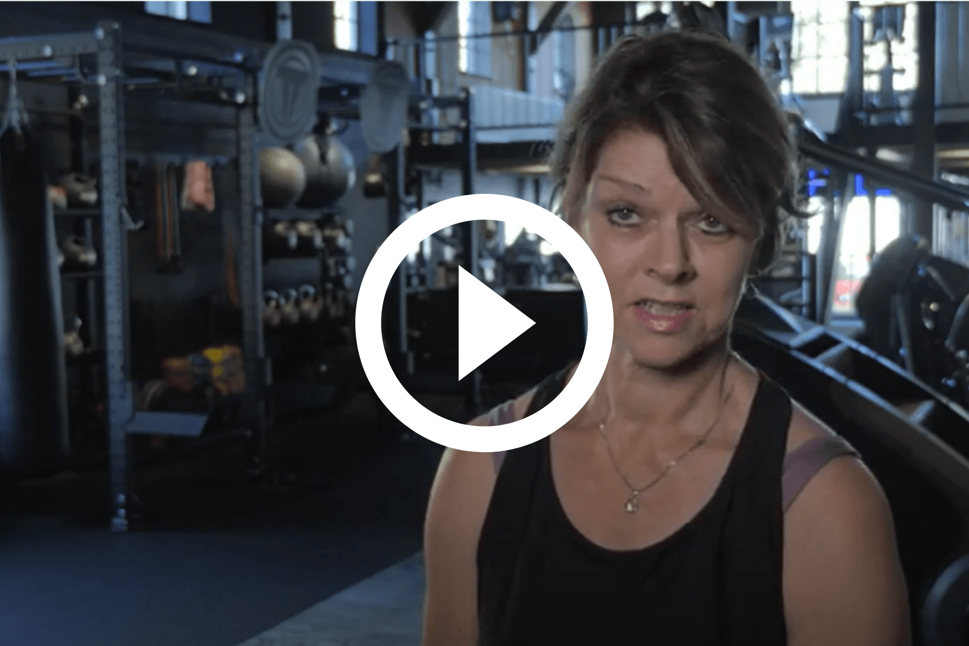 Vrouw in een zwarte top in een industriële omgeving, met een video-afspeelknop eroverheen.