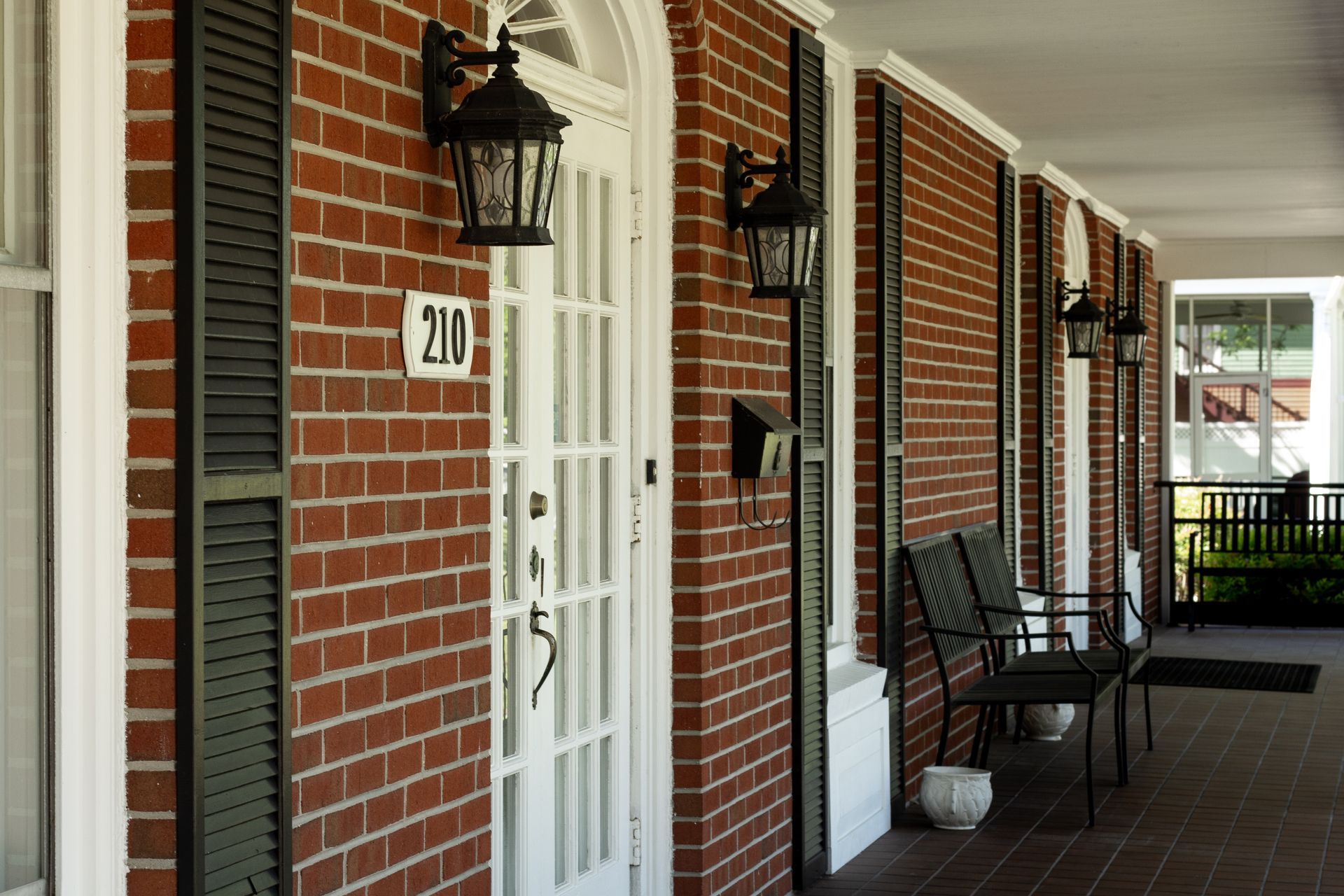 Brick apartment walkway with white doors, black lanterns, and a bench under a covered porch