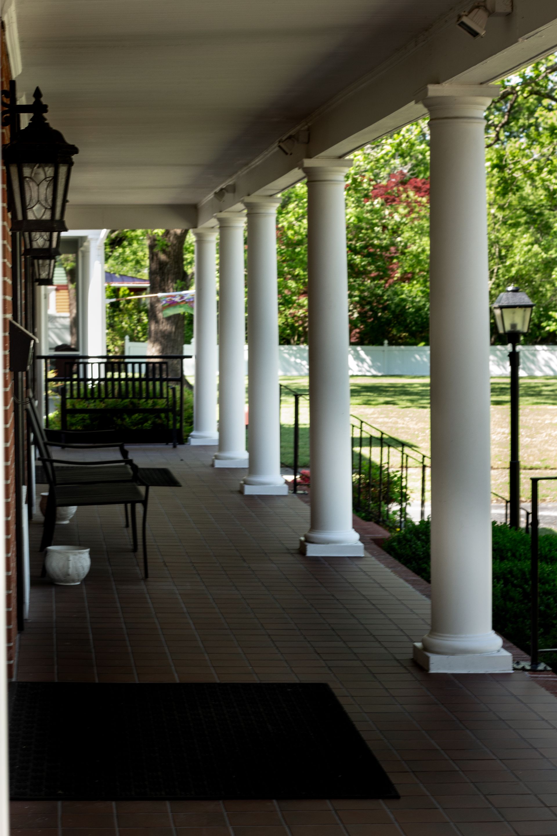 Covered porch with white columns, black railings, and potted plants overlooking a green yard