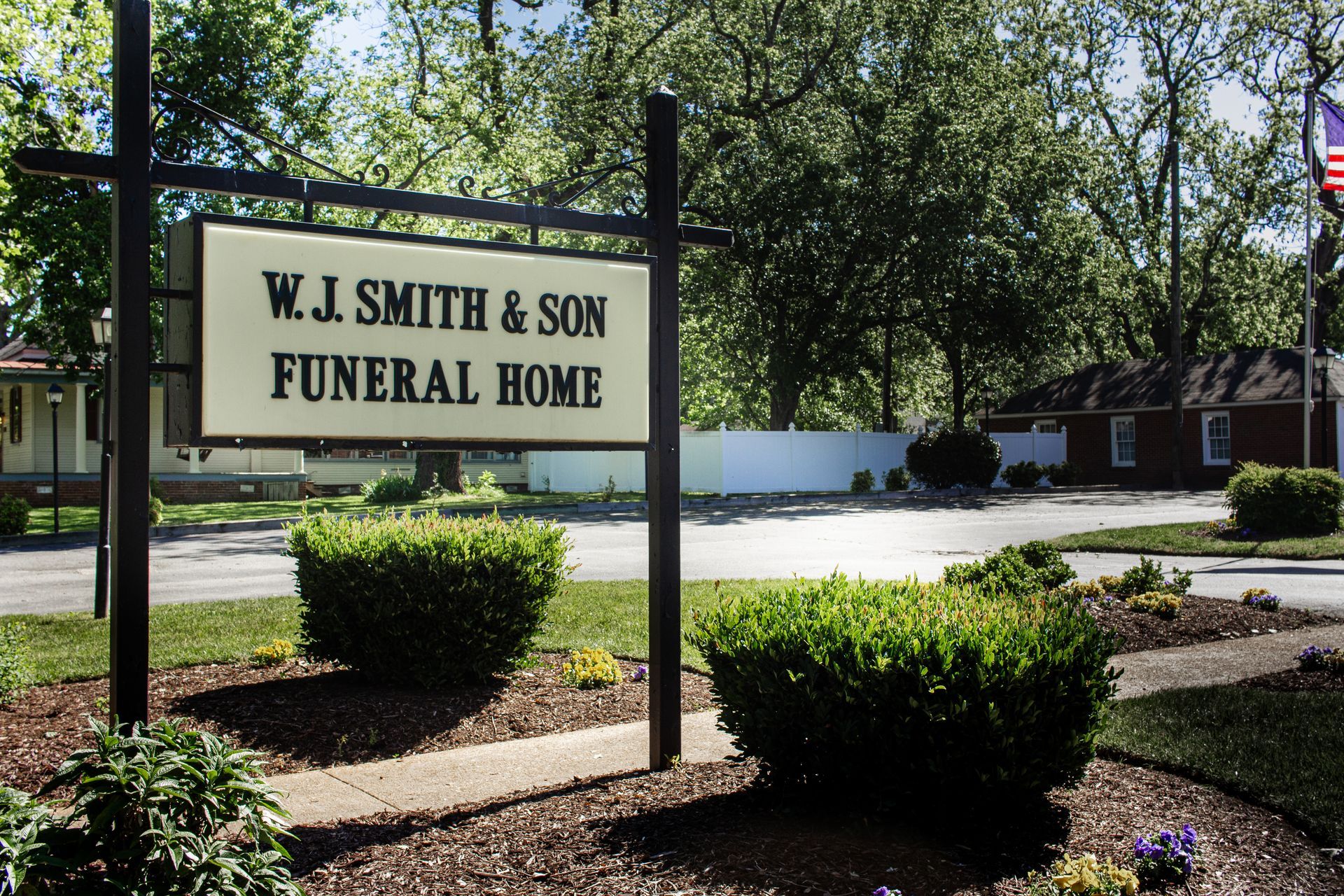 W.J. Smith & Son Funeral Home sign in a landscaped roadside lot, with trees and shrubs around it