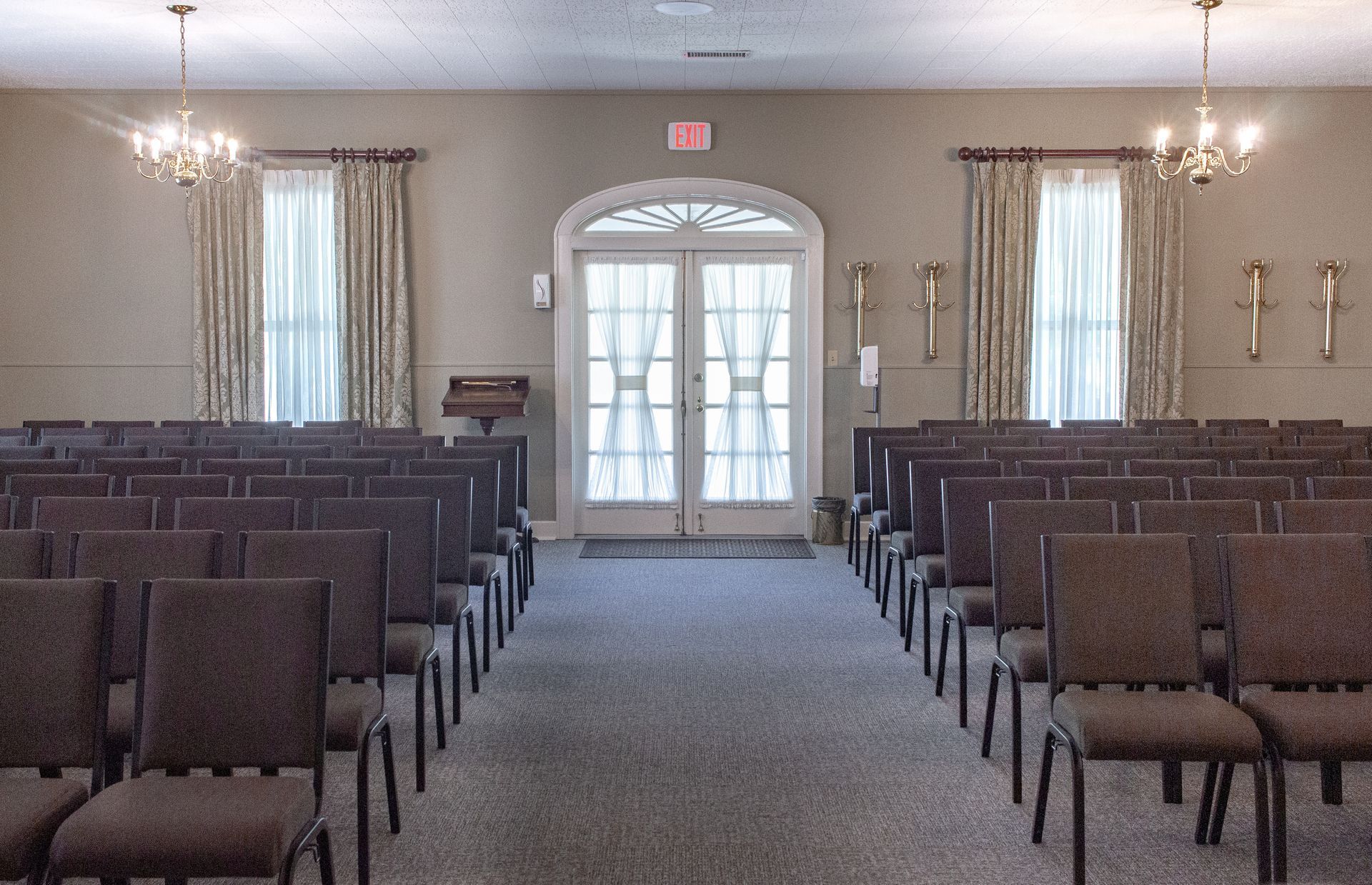 Empty banquet hall with rows of chairs facing double glass doors and chandeliers overhead