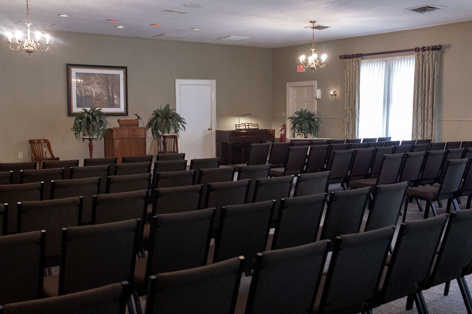 Empty meeting room with rows of black chairs, framed wall art, and a window with curtains