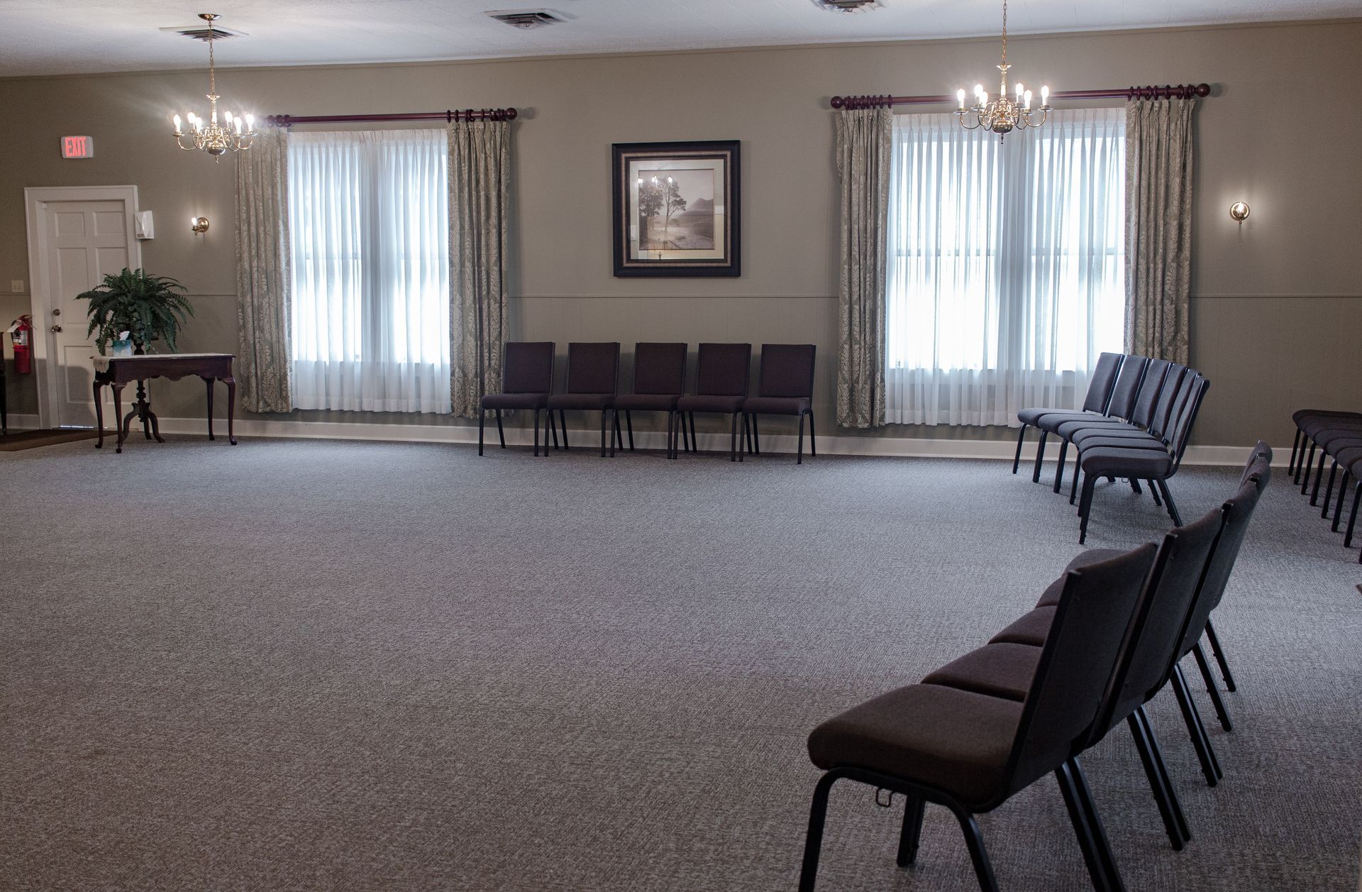 Empty carpeted banquet room with chairs along the walls and windows with curtains