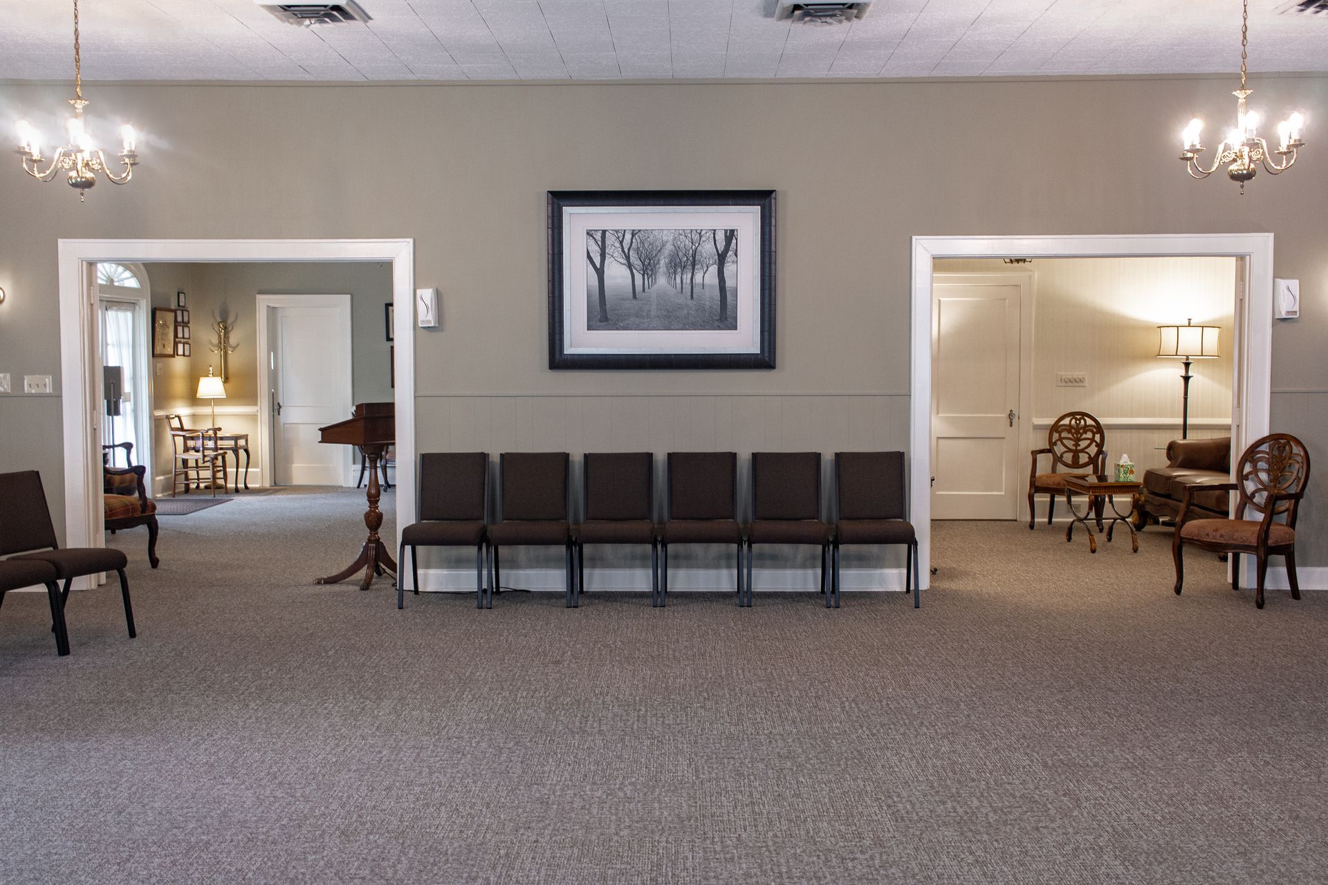 Spacious waiting room with rows of chairs, gray carpet, framed wall art, and open doorways to adjacent rooms