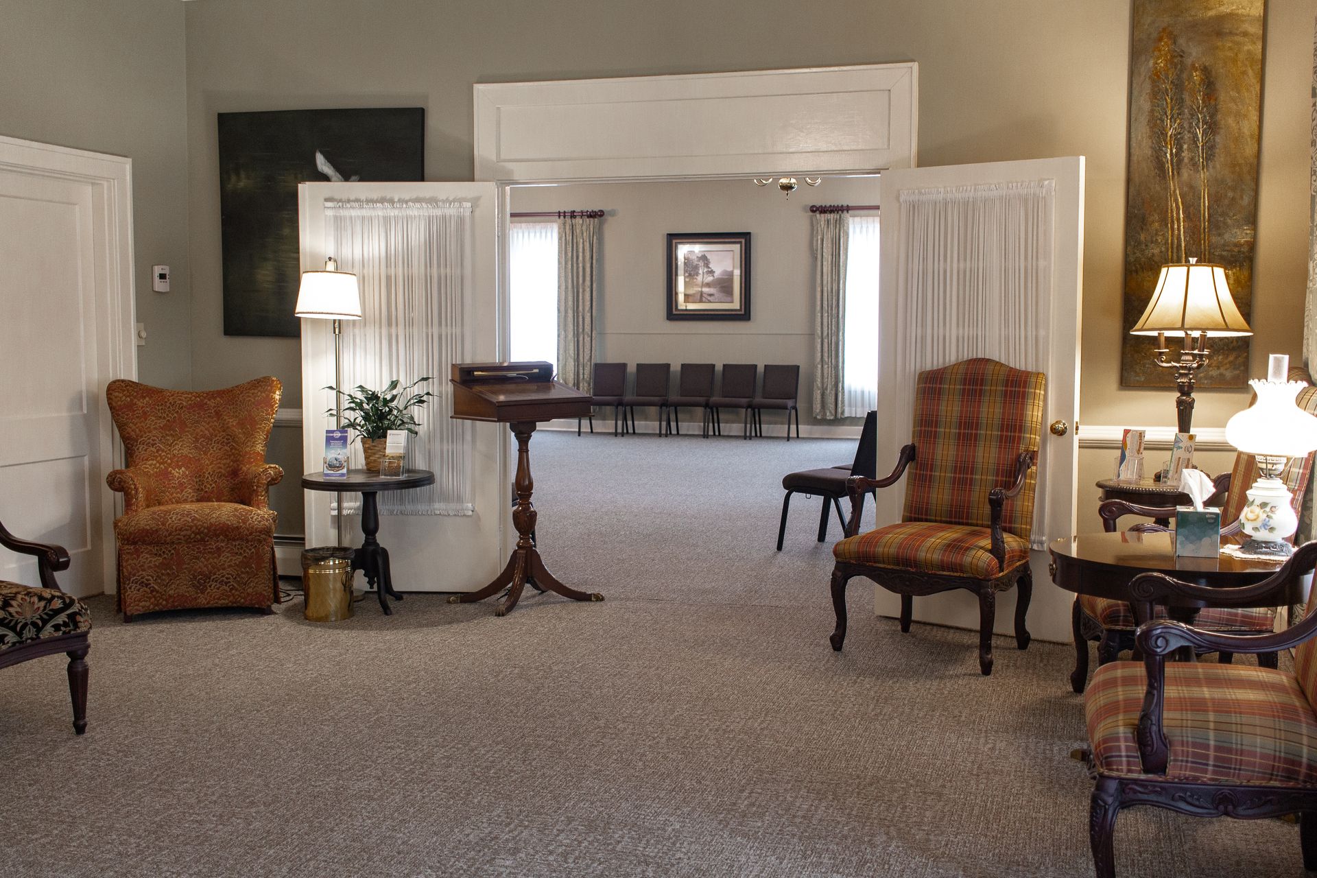 Elegant living room with carpet, chairs, table lamps, and white-draped open doorways