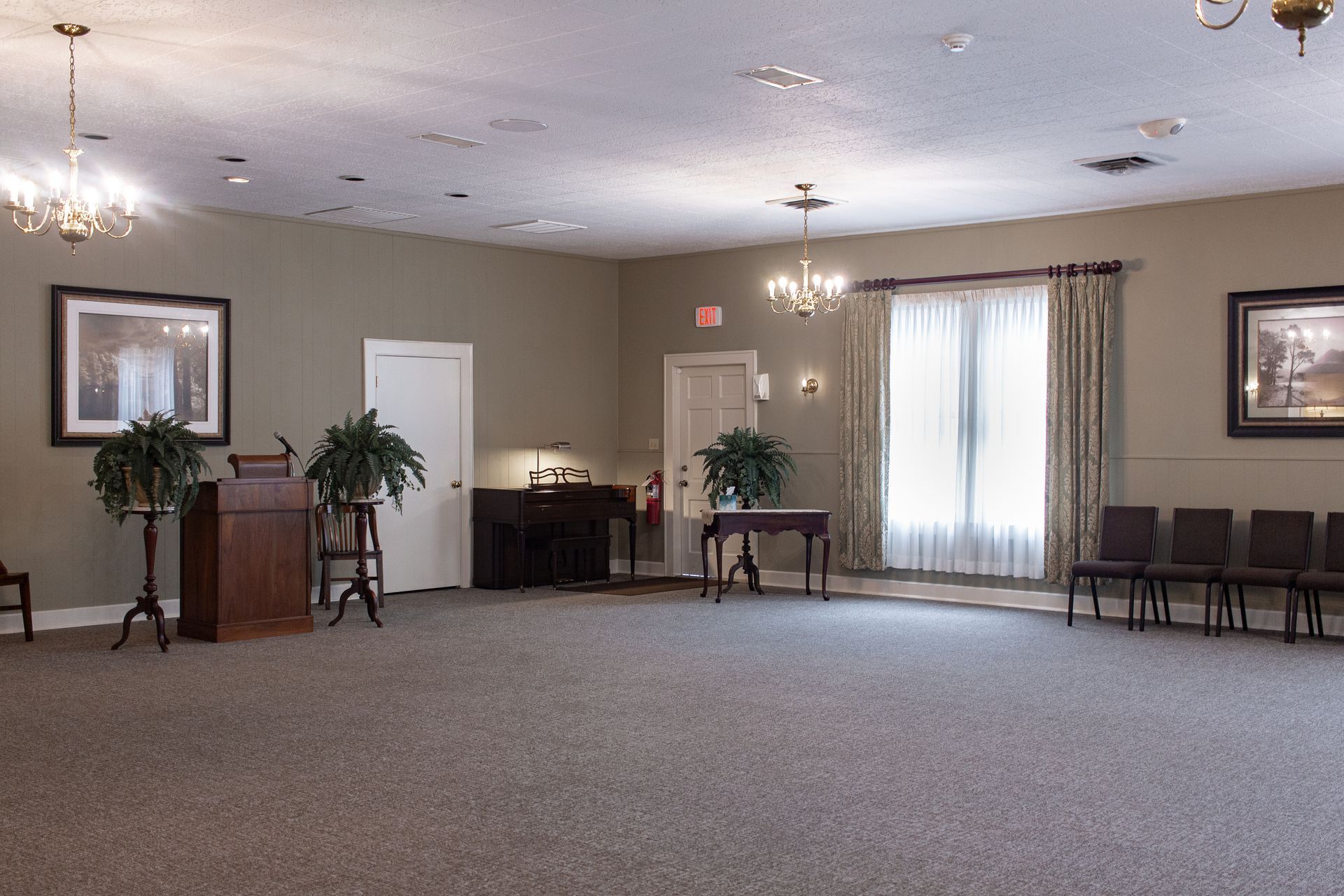 Empty banquet room with beige walls, carpet, chairs, tables, and a bright curtained window.