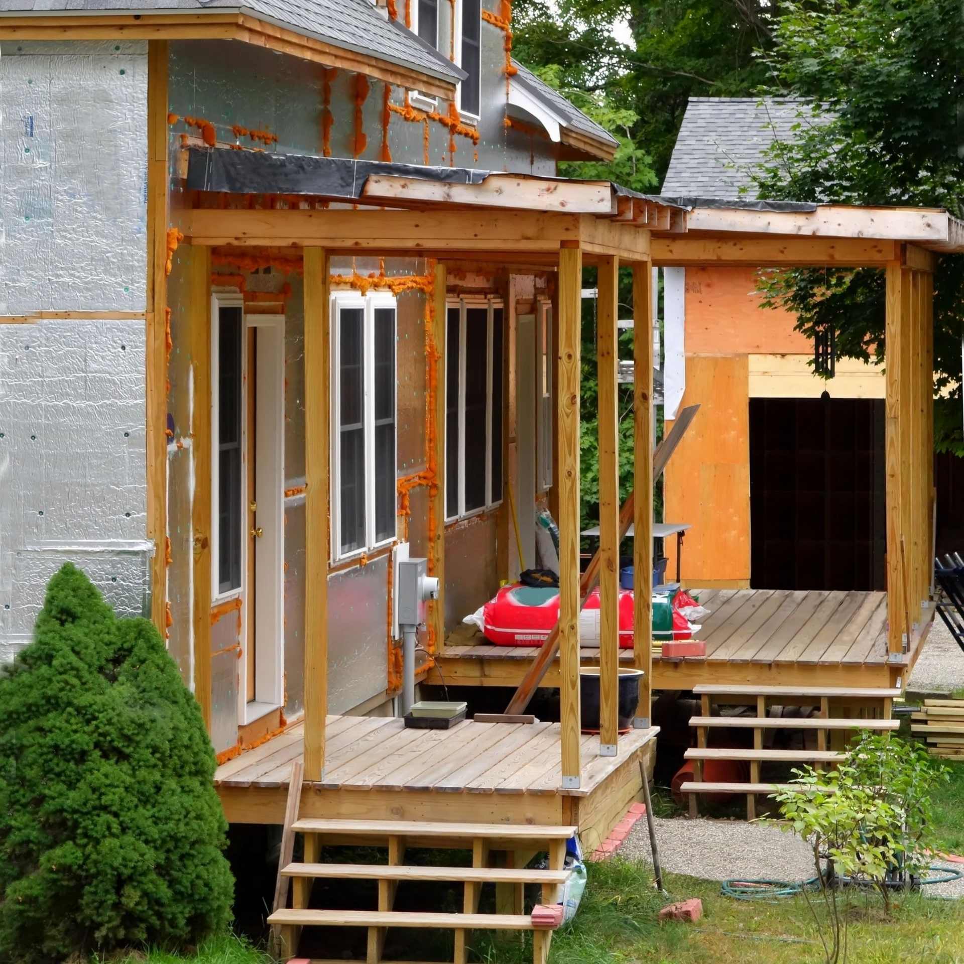 House under construction with a wooden porch and steps. Exterior walls are exposed.