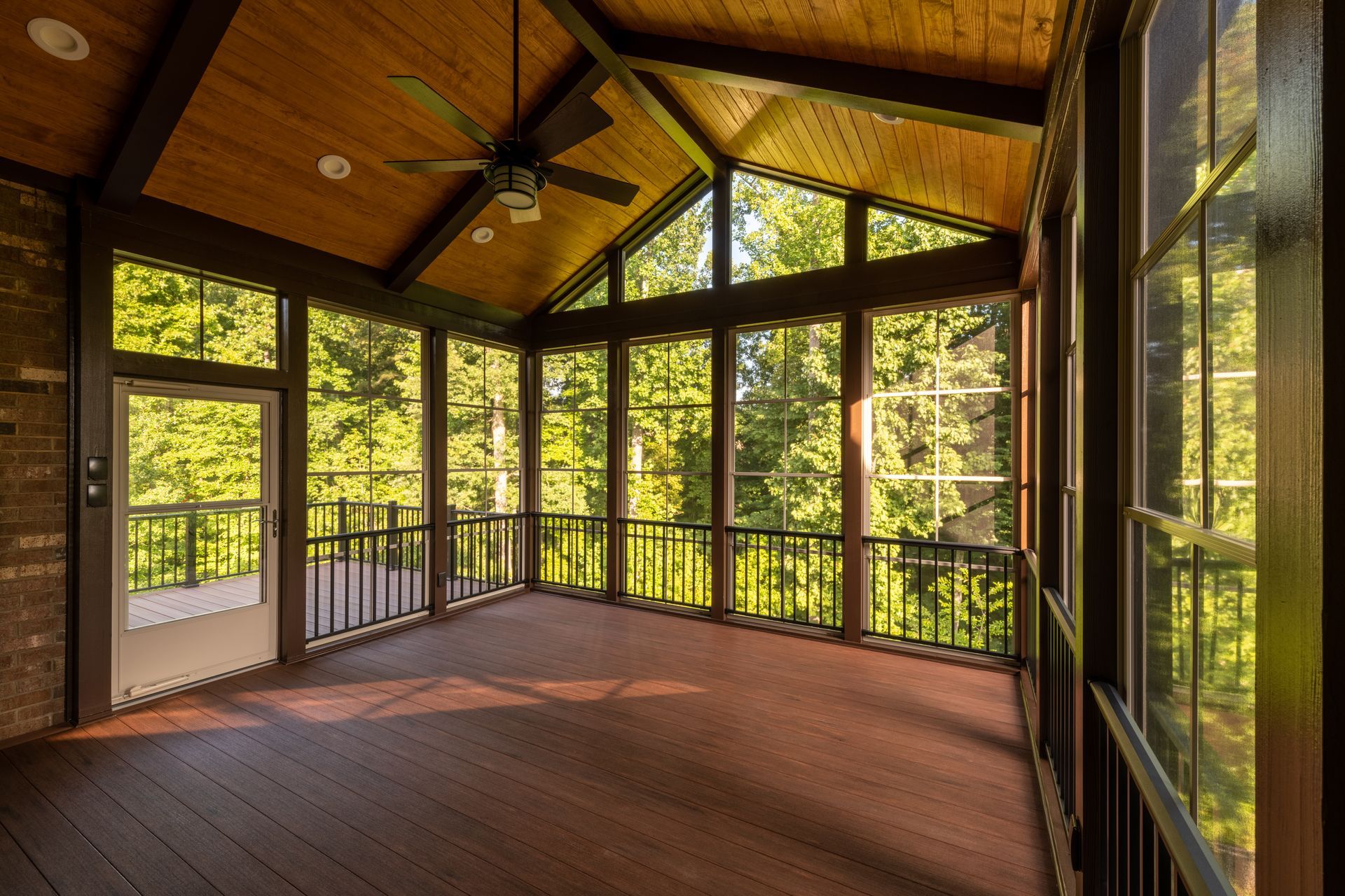 Screened porch with dark wood trim, large windows, and a ceiling fan, overlooking trees.