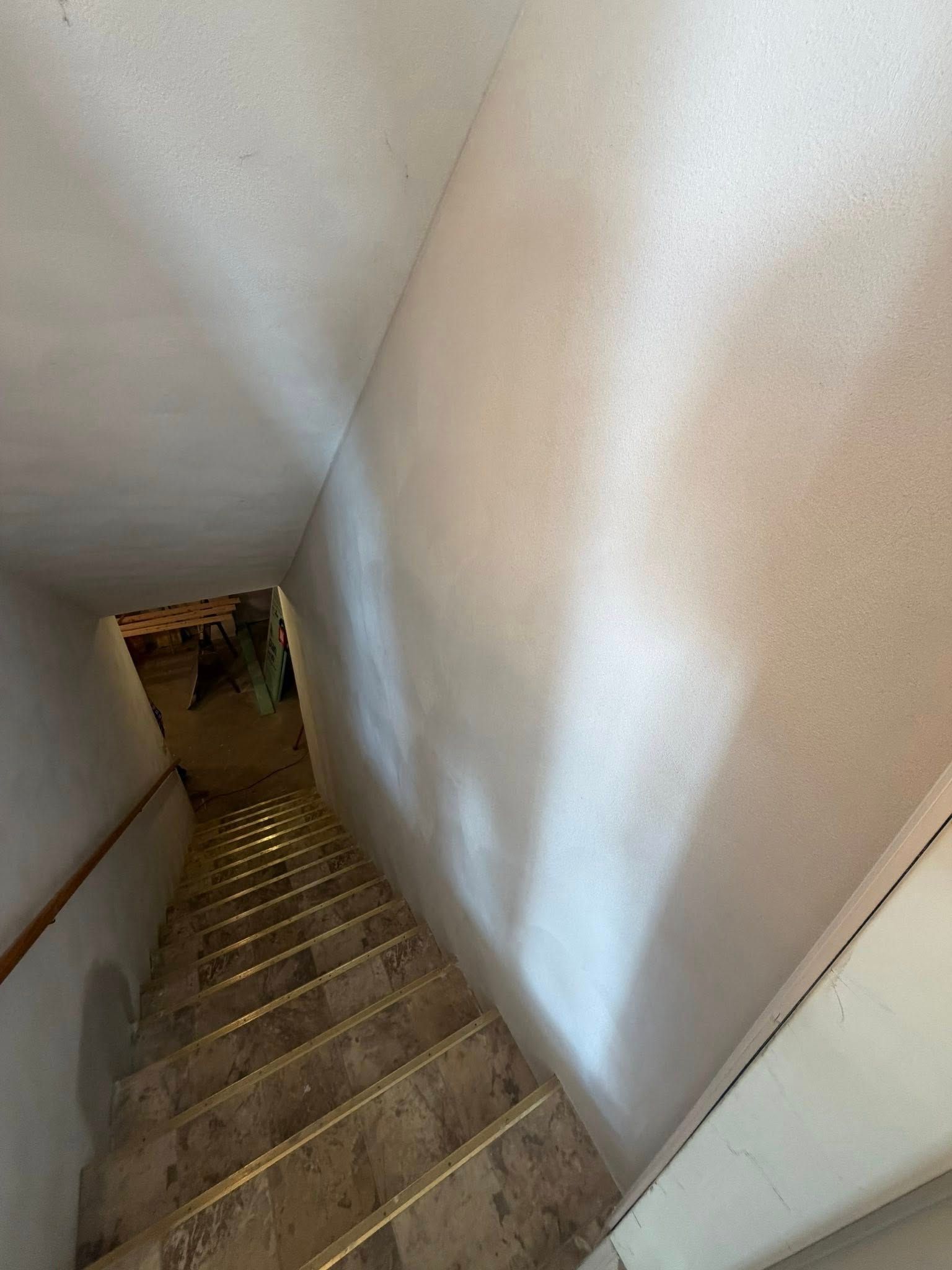 A high-angle view looking down a narrow indoor staircase with beige tile steps, gold trim, and plain light-colored walls.