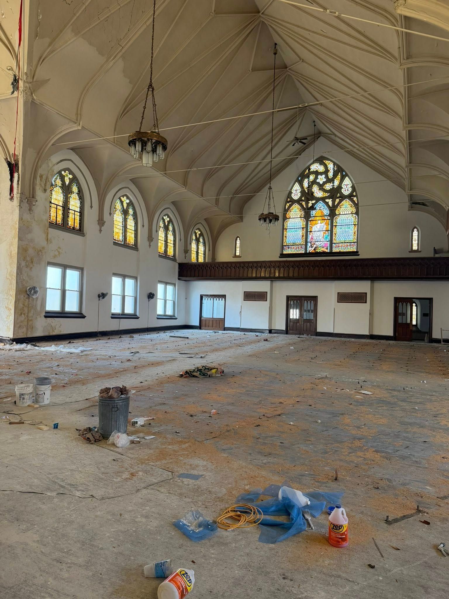 Interior of a dilapidated church featuring a vaulted ceiling, stained glass windows, and debris scattered across the floor.