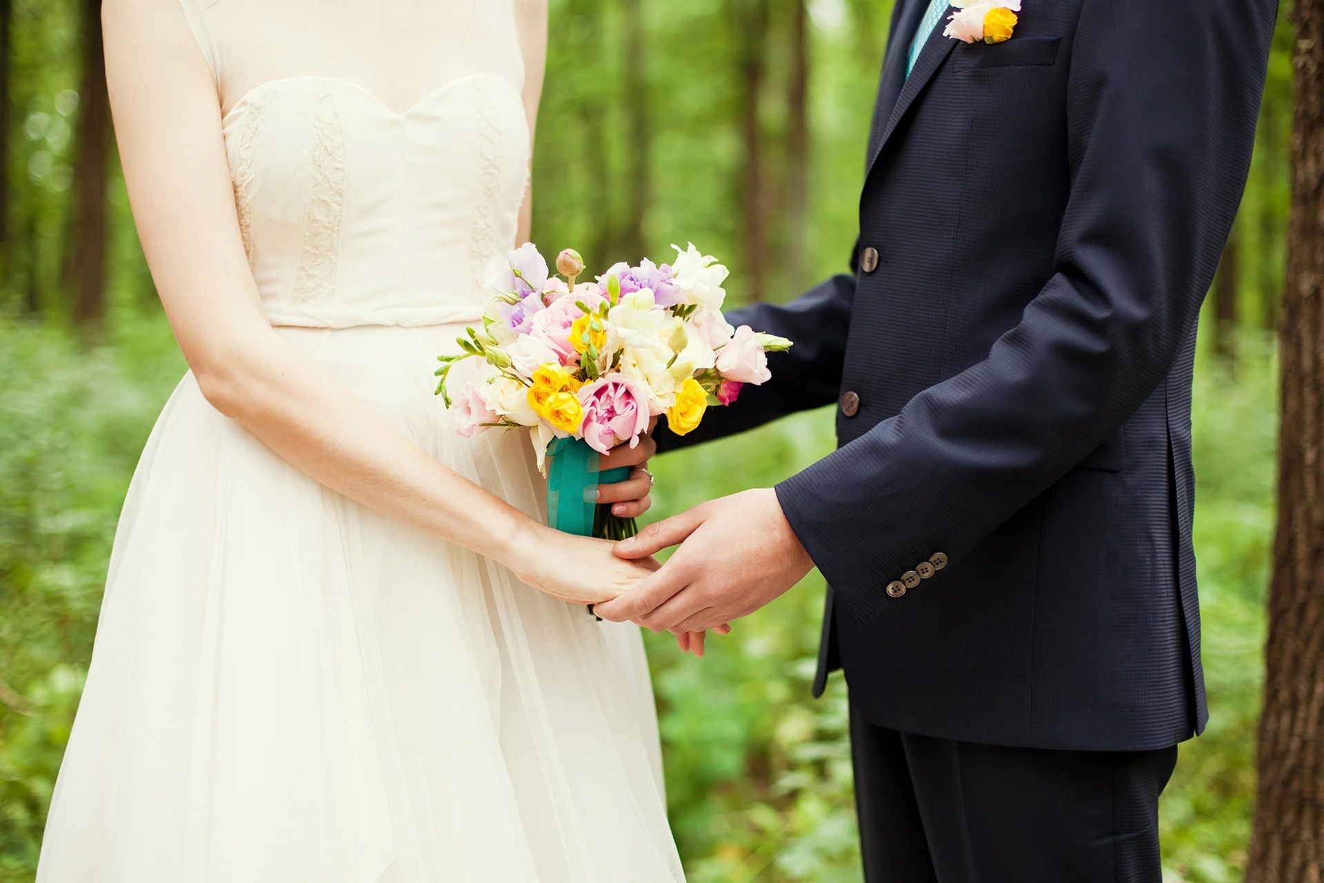 Une mariée et un marié se tiennent la main dans les bois. la mariée tient un bouquet de fleurs.