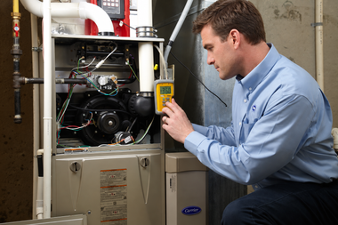Technician inspecting a furnace with a yellow meter in a utility room