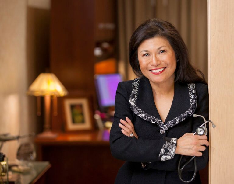 A woman in a black suit is holding a stethoscope and smiling