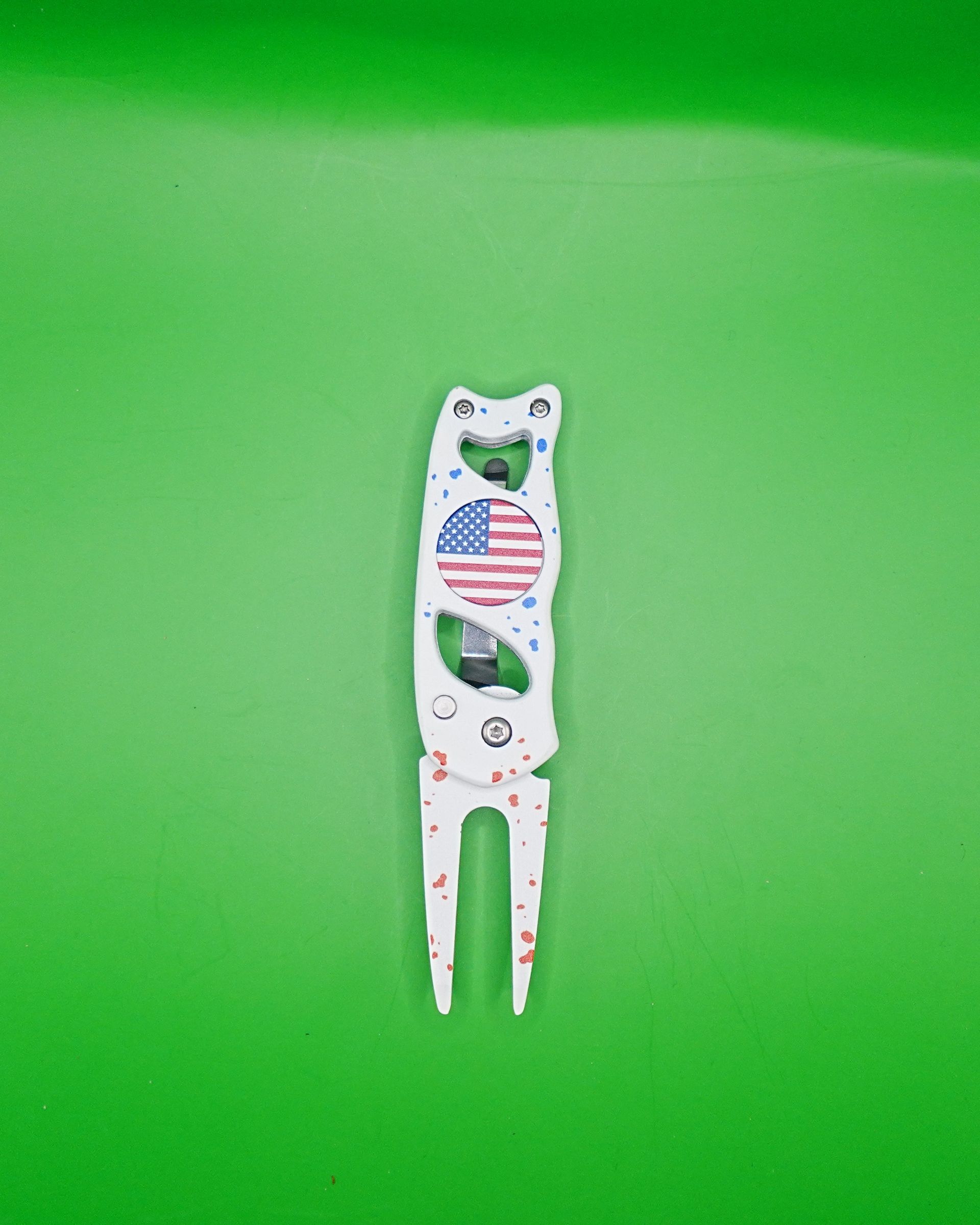 Golf divot repair tool with American flag design on green background.