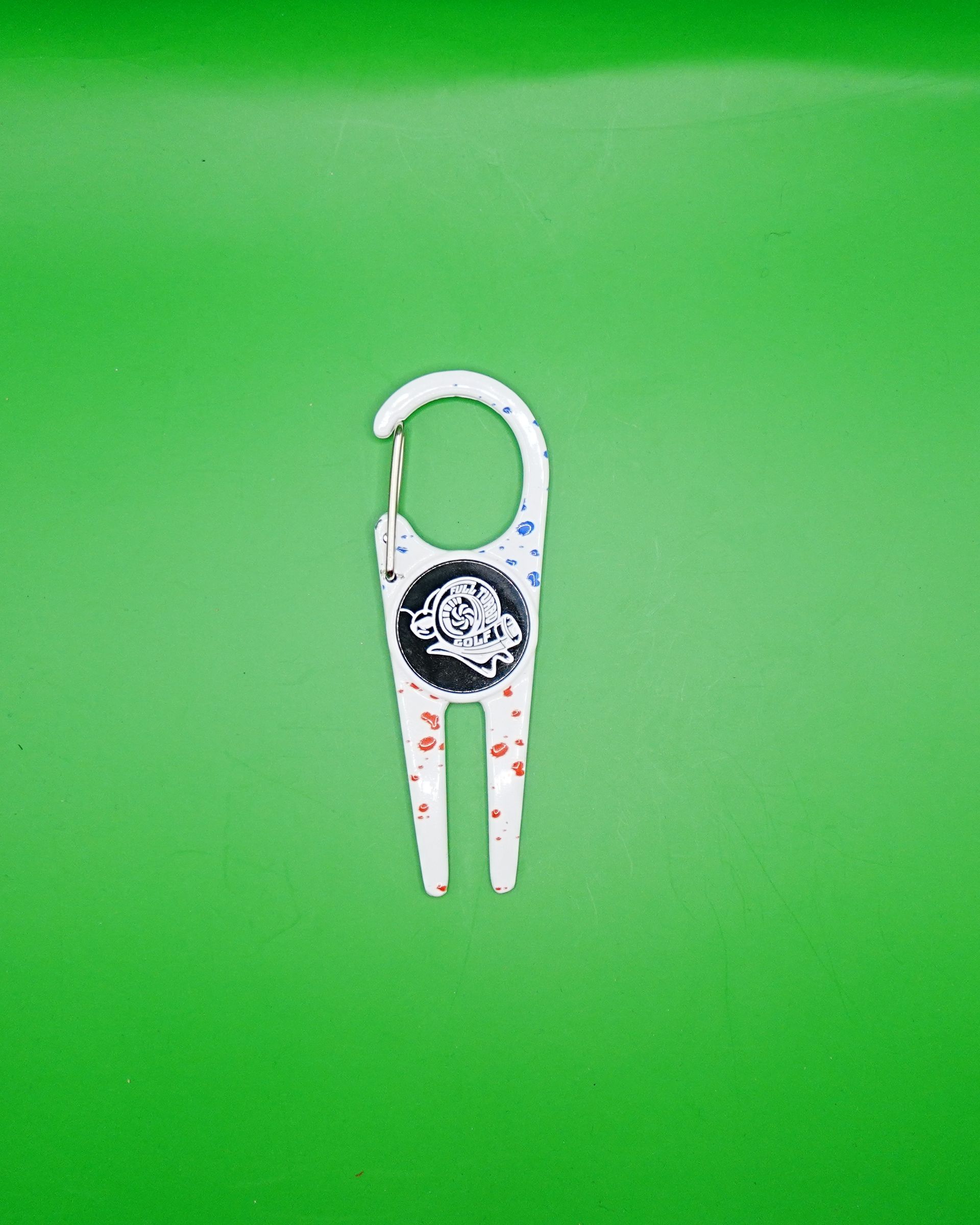 White golf divot repair tool with a metal clip and a logo on a green background.