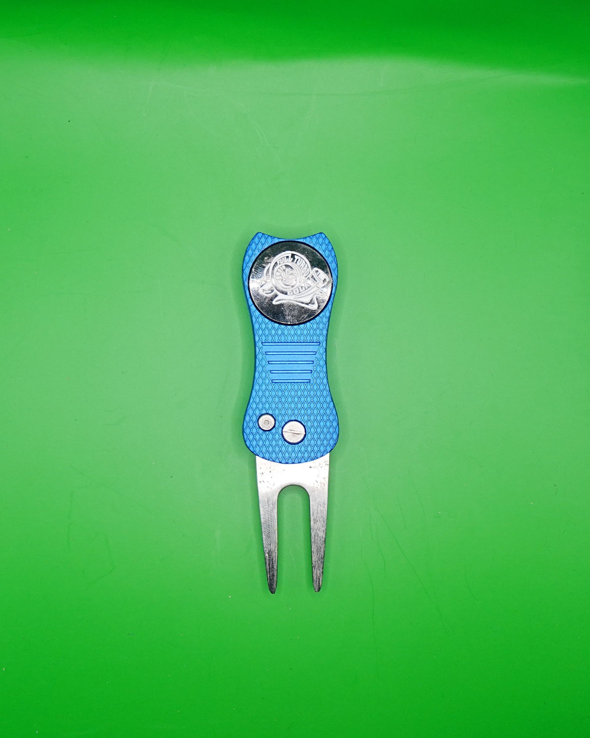 Blue golf divot repair tool with a ball marker on a green background.