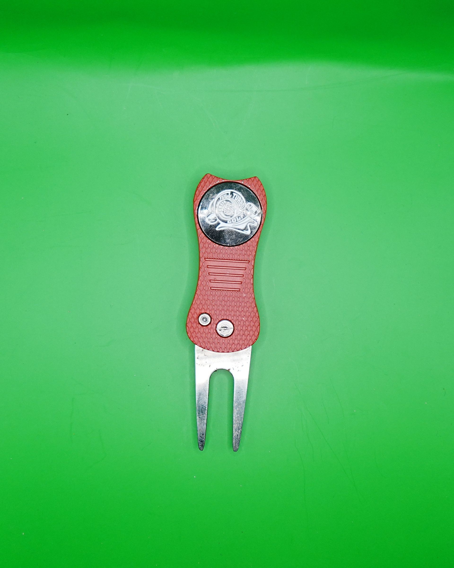Red and white golf divot repair tool on a green background.