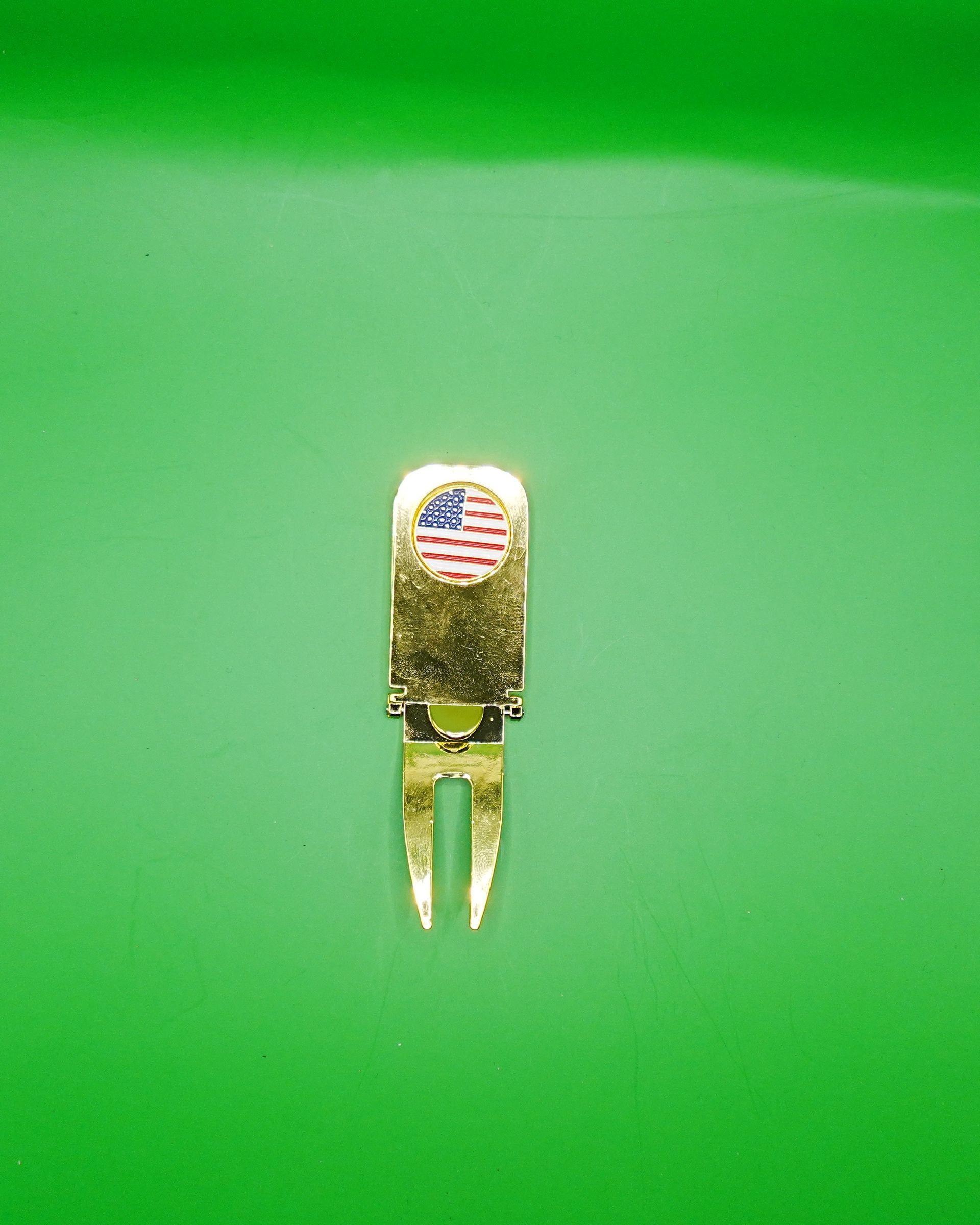Gold golf divot repair tool with American flag detail on a green surface.