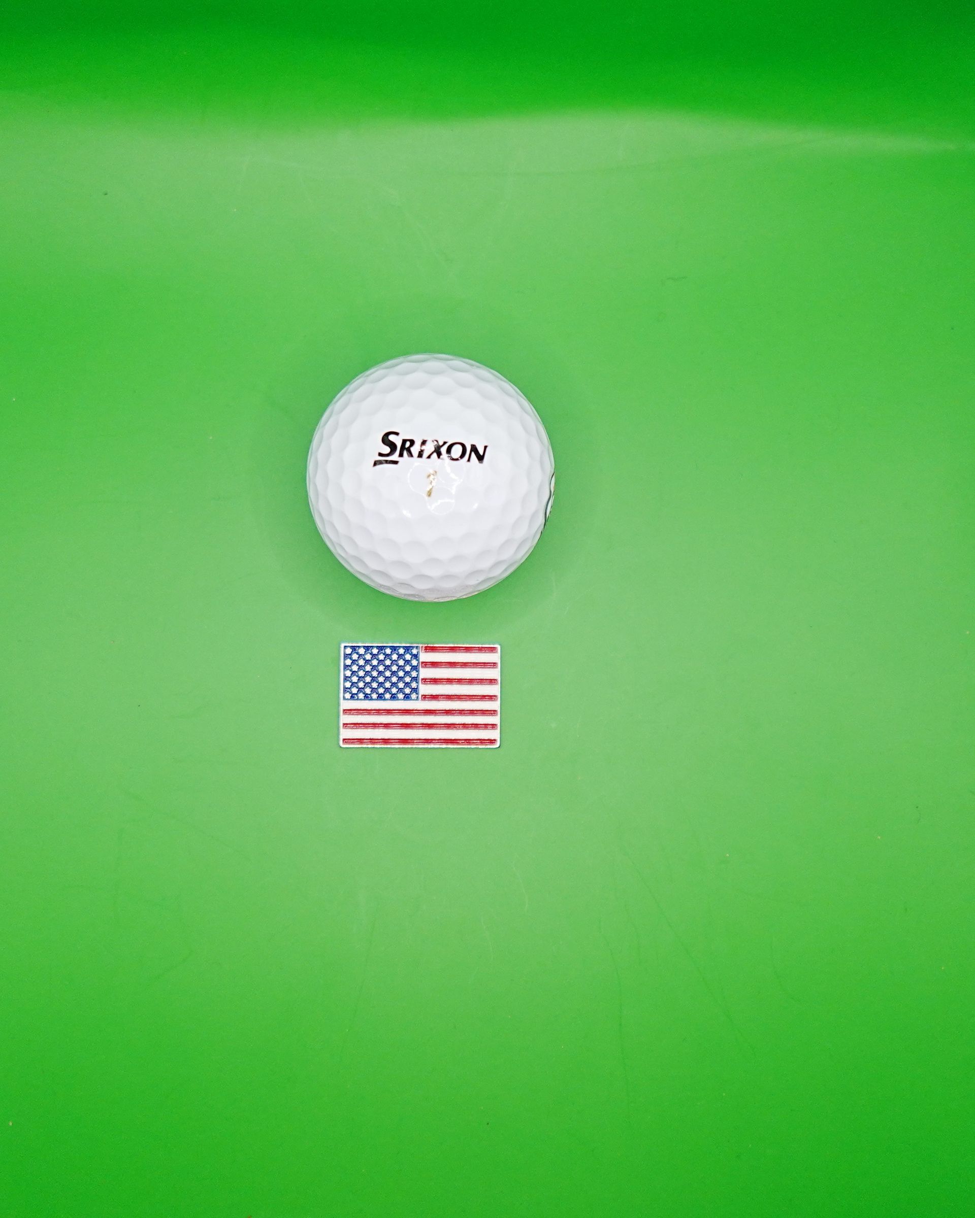 White Srixon golf ball and small American flag on a green surface.