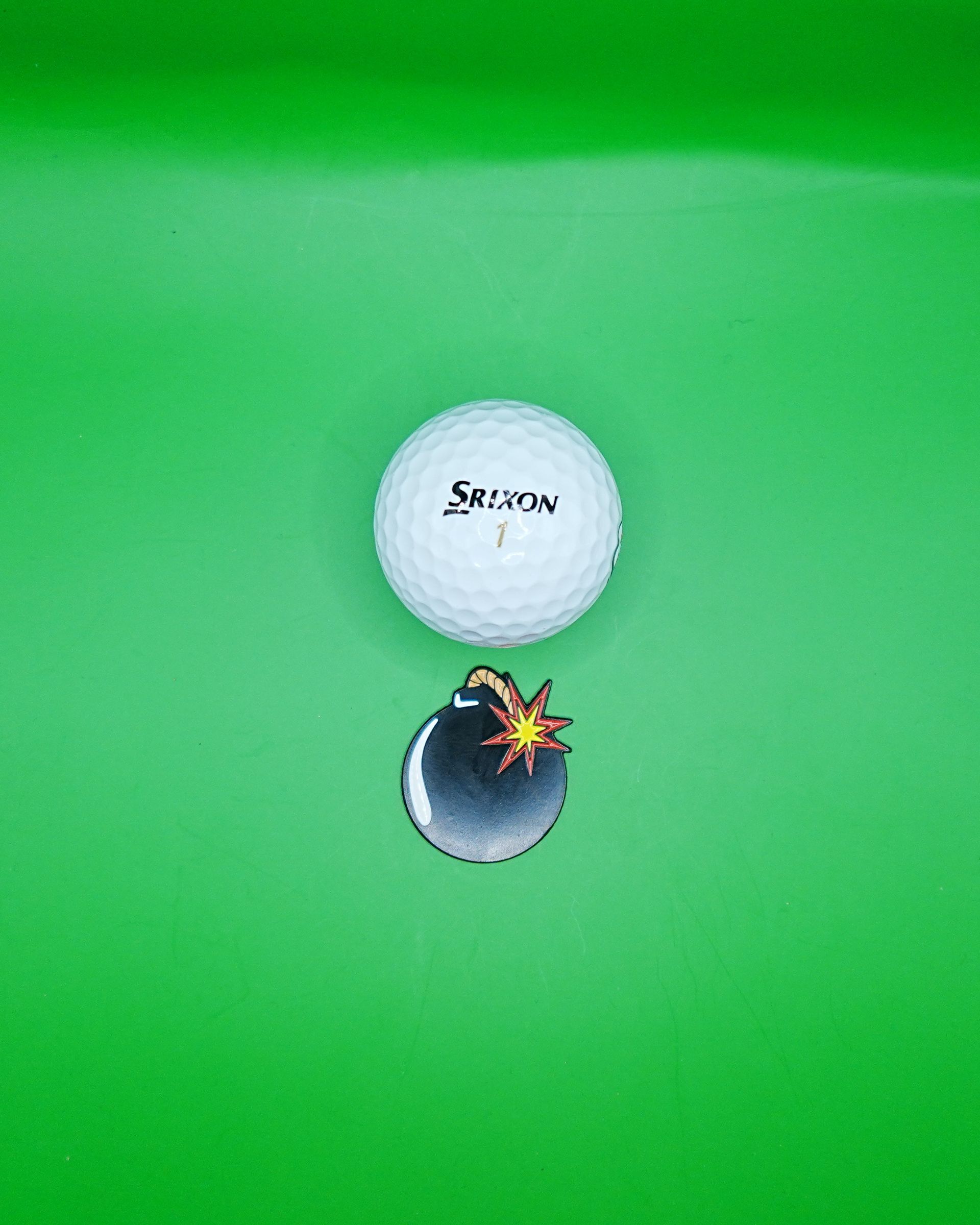 White golf ball and a cartoon bomb on green surface.