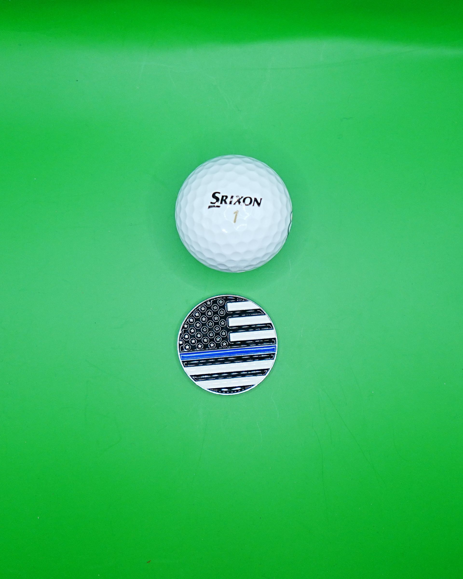 White golf ball and a thin blue line flag golf marker on a green background.