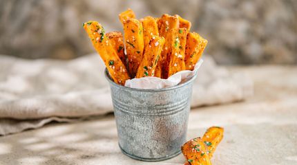 Orange seasoned fries in a small metal bucket on a rustic tablecloth.