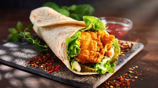 Wrap with crispy fried chicken, lettuce, and sauce on a dark slate board with chili flakes.