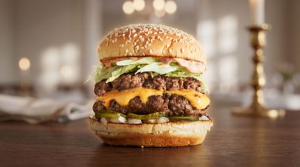 Close-up of a cheeseburger with sesame bun, melted cheese, lettuce, and onion on a wooden table.