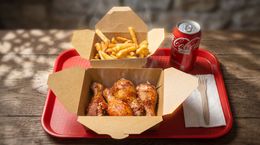 Takeout meal tray with chicken, fries, napkins, and a can of Coca-Cola on a wooden table