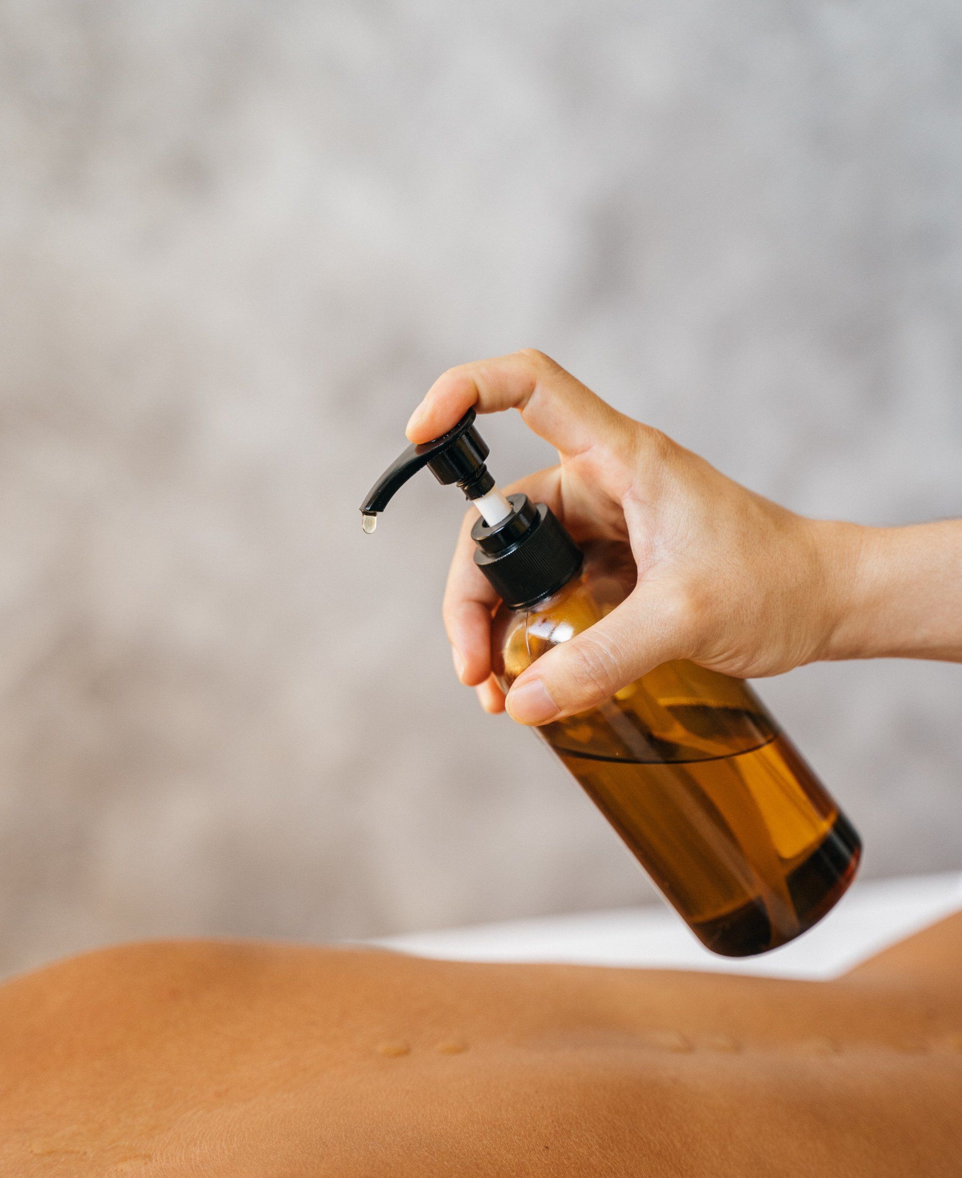 Hand dispensing oil from a brown bottle onto a person's back, setting is neutral.