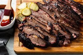 Sliced grilled steak on a wooden board with pickles and dipping sauce