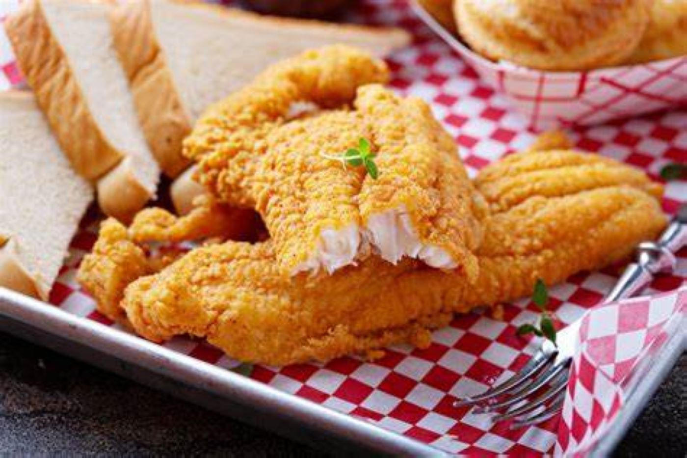 Golden fried fish fillets on a red-and-white checkered tray with lemon slices and forks