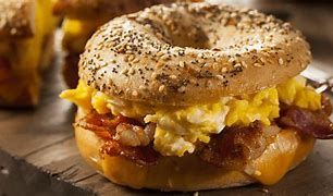 Everything bagel breakfast sandwich with egg, bacon, and melted cheese on a wooden board