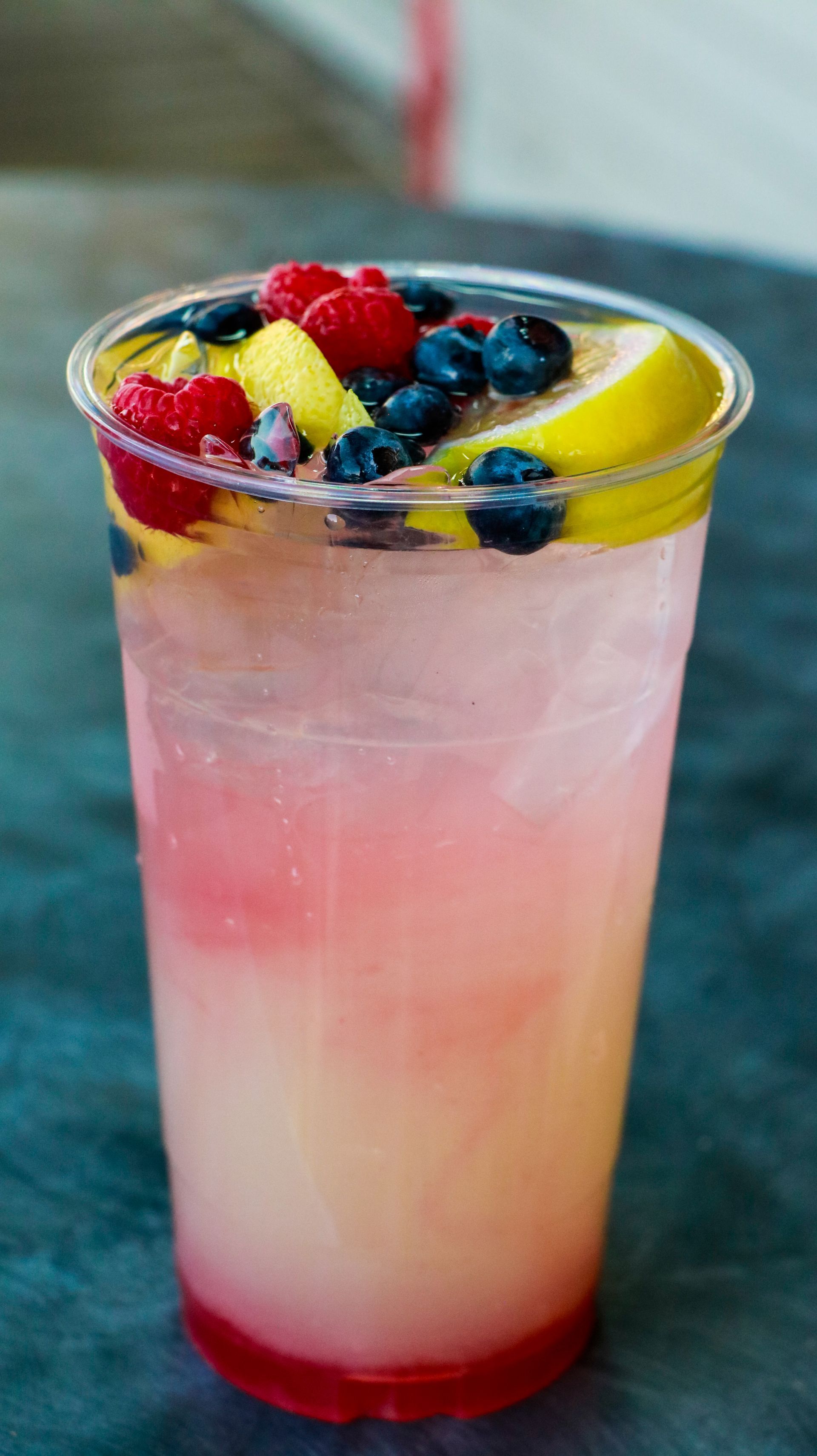 Tall pink fruit cocktail in a clear glass with berries, lemon slice, and ice