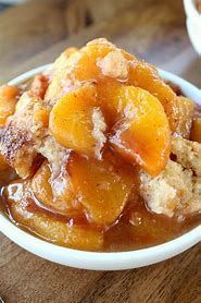 Bowl of peach cobbler topped with syrup on a wooden table