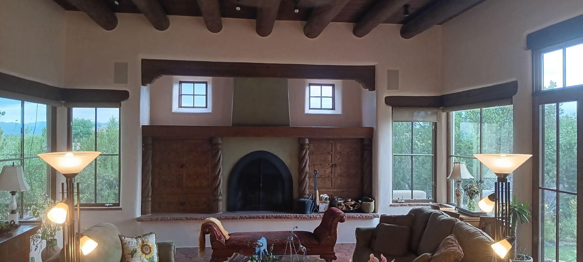 Spacious living room with a large brick fireplace, skylights, and floor-to-ceiling windows overlooking trees
