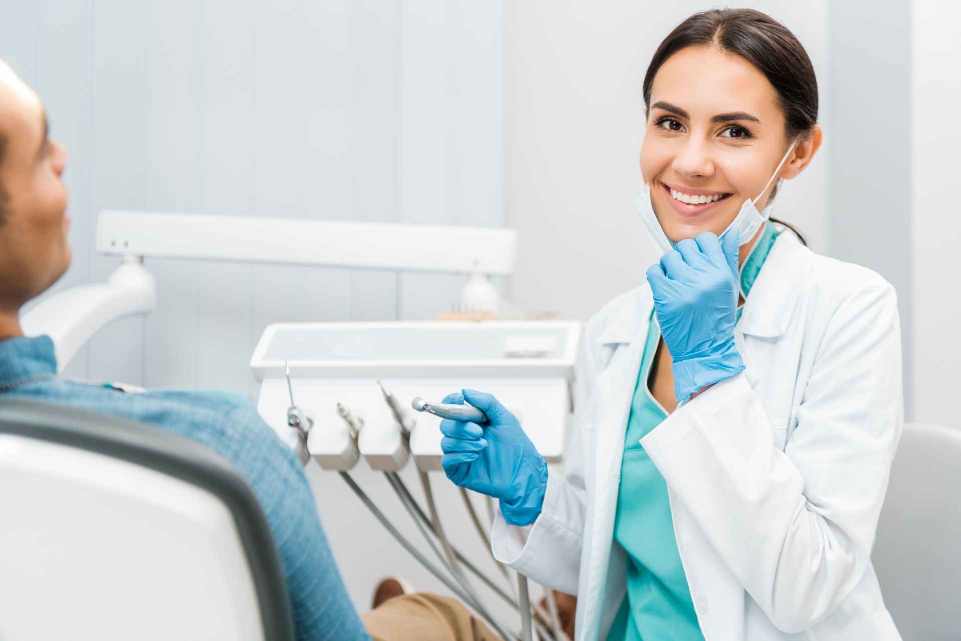 Dentist smiling warmly, patient seated in chair, tools visible in clinic. Dentist smiling warmly, patient seated in chair, tools visible in clinic.