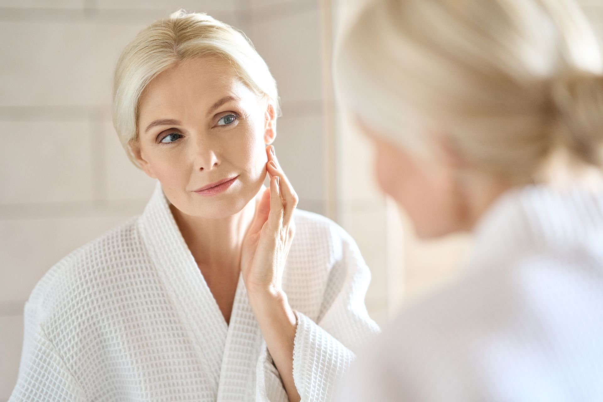 a woman in a white robe is looking at her face in the mirror