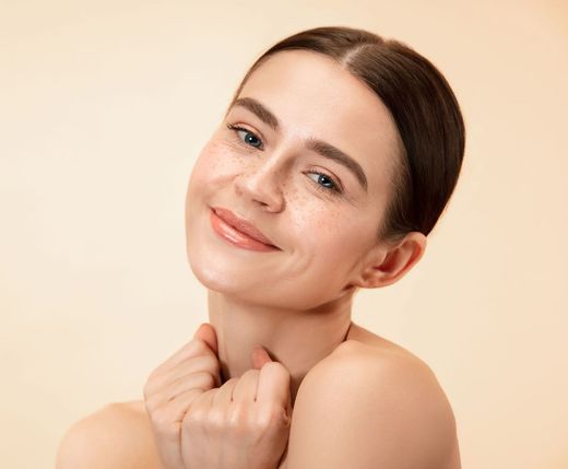 a woman with freckles on her face is smiling and touching her neck