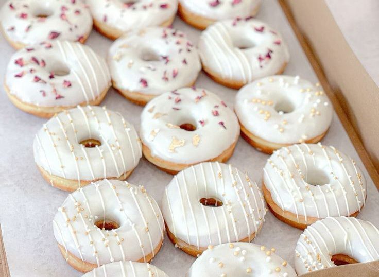 Una caja llena de donas glaseadas de color blanco con chispas.
