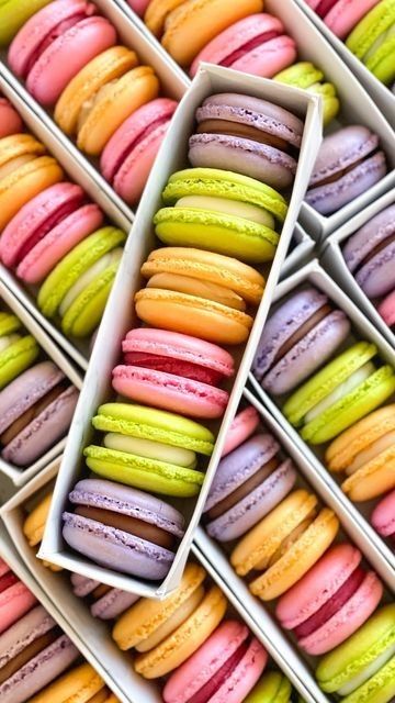Un montón de macarons coloridos se apilan uno encima del otro en cajas.