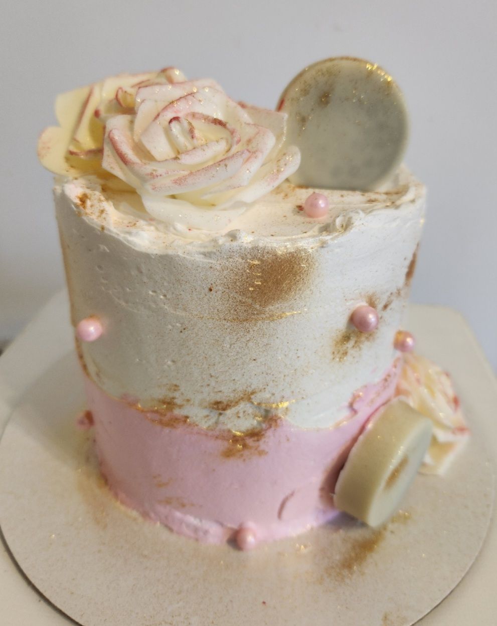 Pastel pequeño de dos niveles con glaseado rosa y blanco, decorado con una rosa, chispas y detalles dorados.