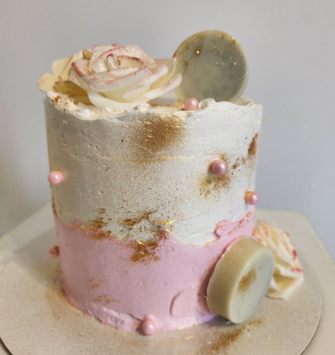 Pastel pequeño de dos niveles con glaseado rosa y blanco, decorado con una rosa, chispas y detalles dorados.