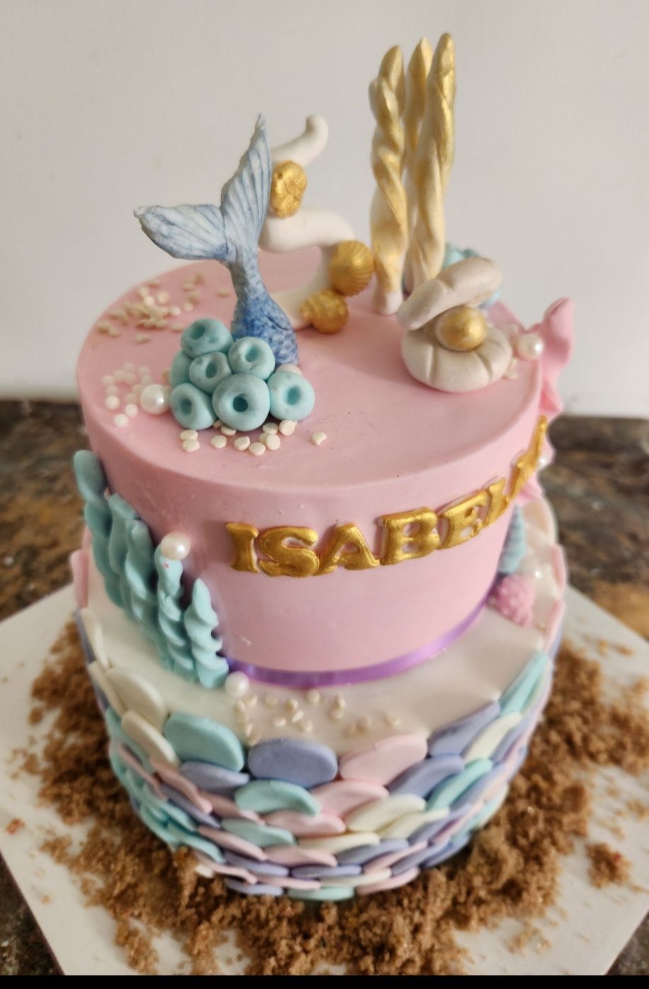 Pastel de dos niveles con temática de sirena con glaseado rosa, cola de sirena, detalles dorados y nombre 