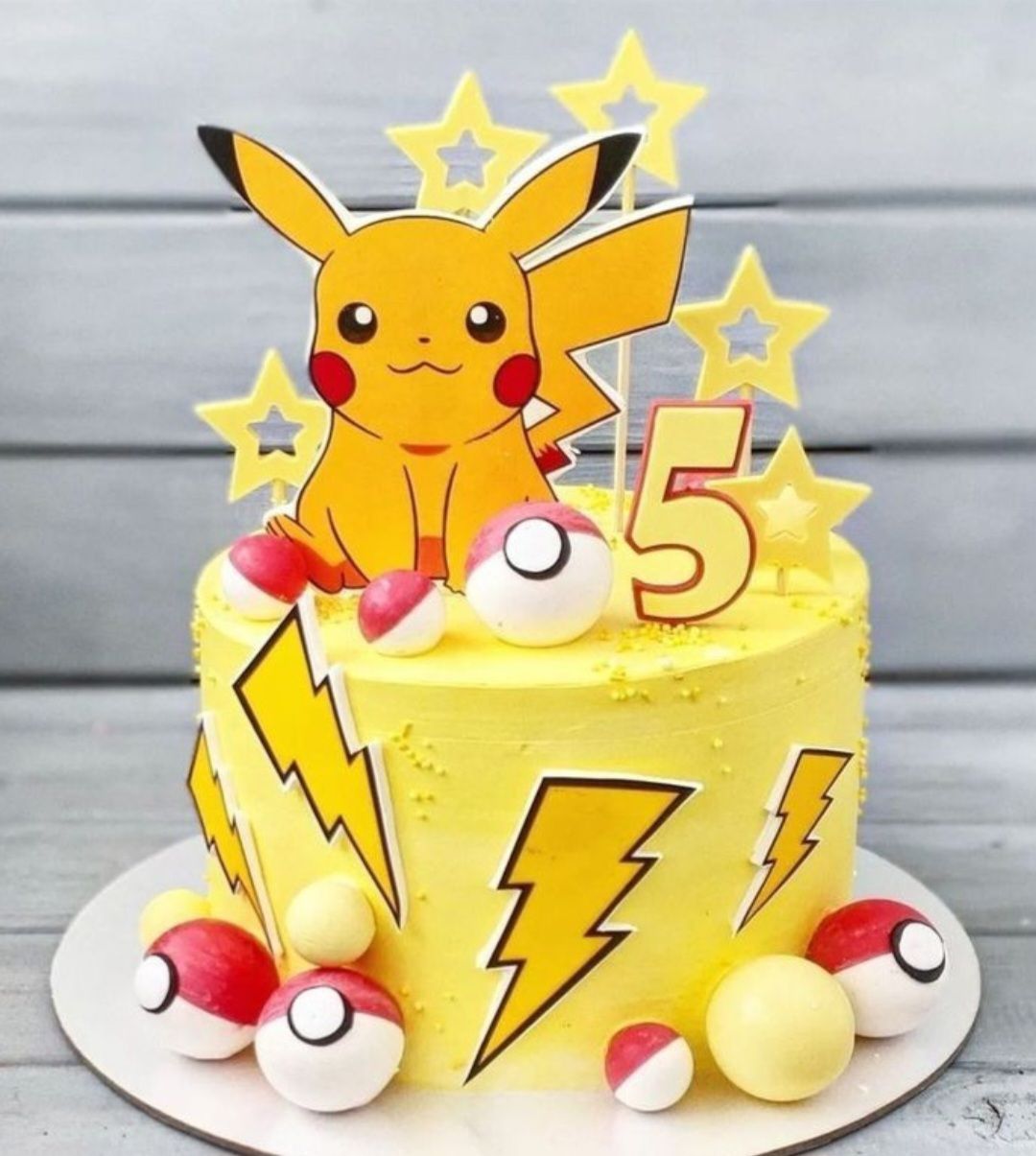 Pastel con temática de Pikachu con glaseado amarillo, orejas negras y una Pokébola sobre un soporte para pastel blanco.