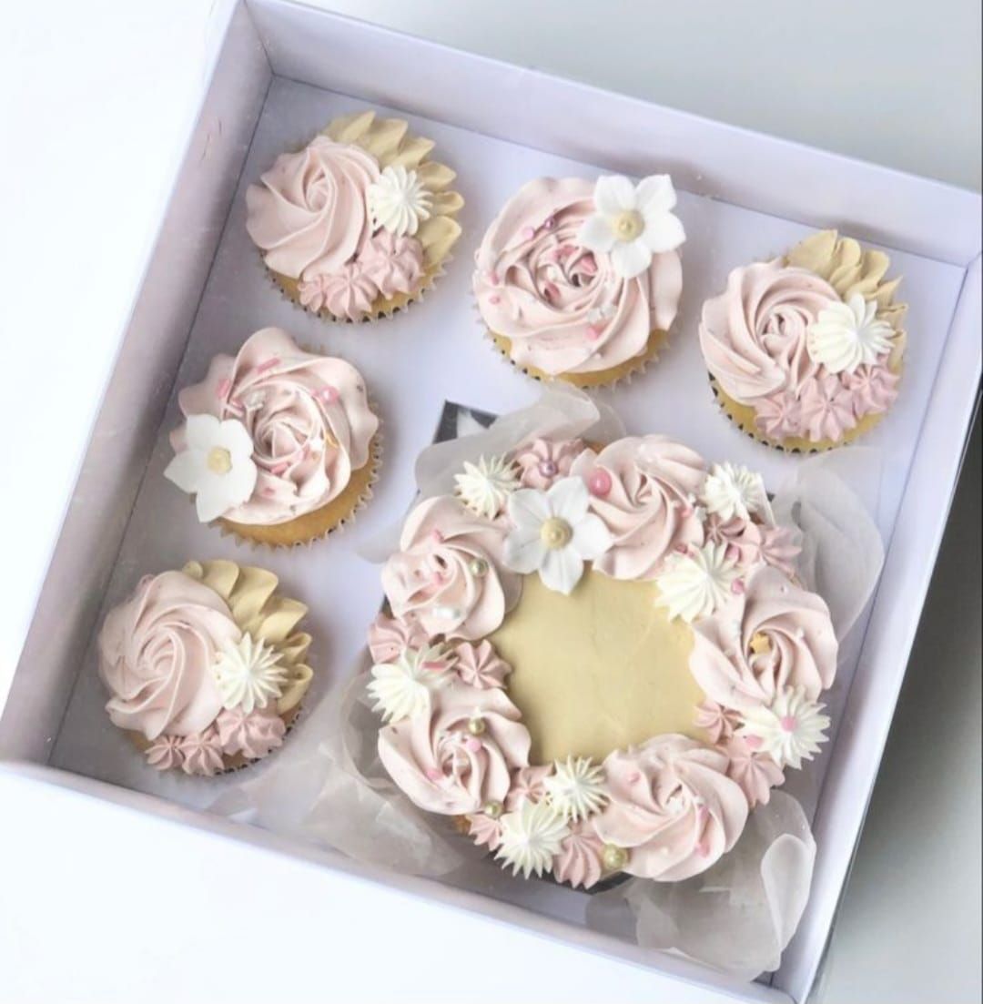 Caja de cupcakes glaseados con diseños florales en tonos rosas y blancos.