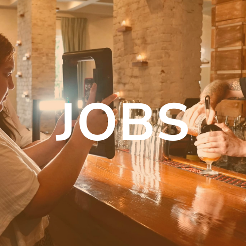 Person using a tablet at a bar, while a bartender pours a beer. The word
