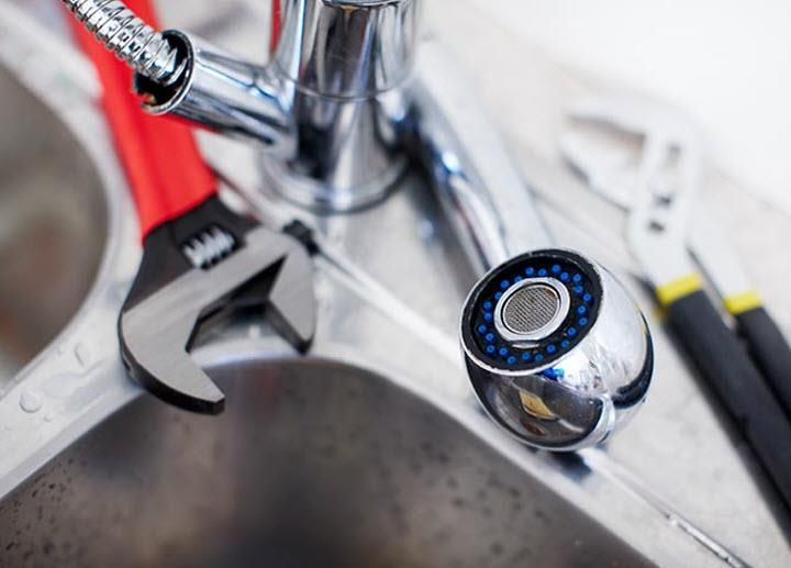 Close-up of a kitchen sink faucet with a blue aerator and a wrench nearby